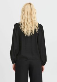 Black long-sleeve blouse with puffed shoulders, featuring a textured fabric and a relaxed fit, worn with tailored black pants.