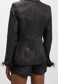Schwarze Blazer mit welliger Textur und metallischen Fadendetails; verfügt über gefiederte Akzente an den Ärmeln, eine taillierte Passform und scharfe Revers.