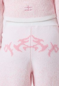 Soft pink knit pants with a lighter waistband and symmetrical darker pink abstract design across the upper hip area.