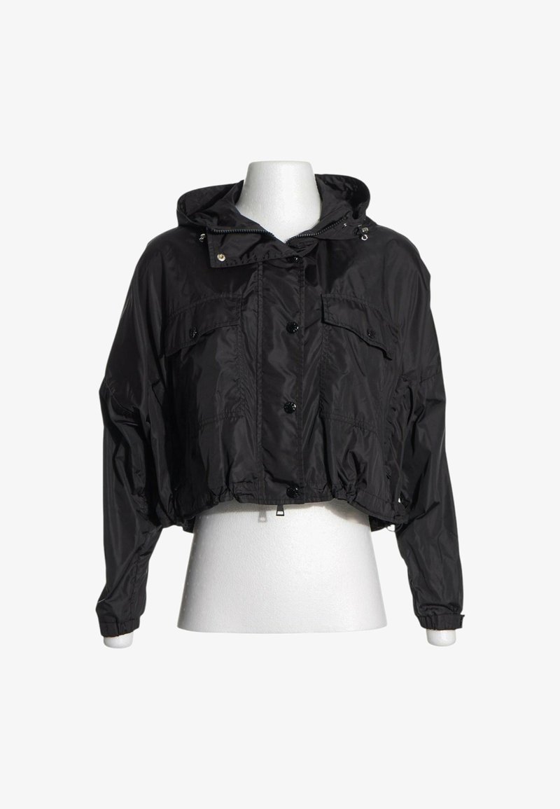 Veste courte noire à capuche avec boutons sur le devant, deux poches poitrine et poignets élastiqués sur un torse de mannequin blanc.