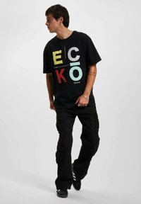 Black oversized T-shirt featuring multicolored "ECKO" graphic. Paired with black cargo pants, offering a relaxed fit and functional pockets.