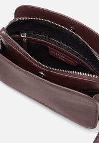 Skórzana torebka na ramię w głębokim bordowym kolorze, wyposażona w przegrody na zamek i fakturowane wykończenie. Wnętrze z czarną podszewką i miejscami na karty.
