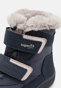 Botas azul-escuro com um suave acabamento em pele cinza, apresentando fechos de Velcro e um logótipo "superfit". Tecido liso e sola de borracha resistente.