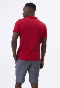 Rød polo-shirt med korte ærmer, flad krave og et enkelt design, parret med grå shorts med en subtil tekstur og lommer.