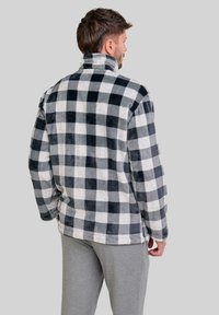 Chaqueta de forro polar en patrón de cuadros en blanco y negro. Cuello alto, corte holgado, textura suave. Pantalones grises visibles en la parte inferior.