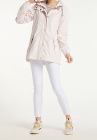 Veste imperméable rose clair avec capuche, dotée de garnitures argentées, deux poches latérales zippées, poignets élastiques et un ourlet arrière légèrement plus long.