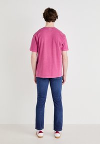 Korte mouwen, ronde hals t-shirt van vervaagd roze stof, gecombineerd met donkerblauwe jeans en sneakers met rode accenten, gezien vanuit de achterkant.