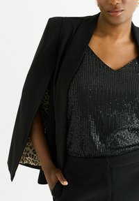 Black blazer with open sleeves, showcasing a leopard print lining. Underneath, a black sequin top with a V-neck design.