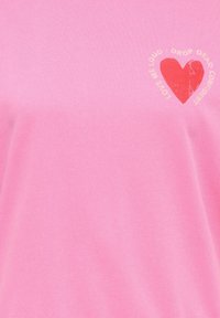 Roosa kangas, millel on väike tuhmunud punane süda ja selle ümber valge tekst "LOVE ME LOUD - DROP DEAD GONNA".