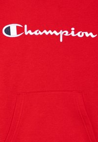 Red sweatshirt made of cotton blend, featuring a front pocket and white embroidered "Champion" logo in cursive at the center.