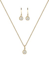 Ensemble de bijoux dorés comprenant un collier chaîne avec un pendentif rond et des boucles d'oreilles à pendants assorties, ornés d'accents circulaires blancs et lisses.