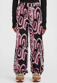Zwart geblokte broek met gedurfde roze en witte abstracte ontwerpen, met een relaxte pasvorm en elastische manchetten, gecombineerd met beige schoenen.