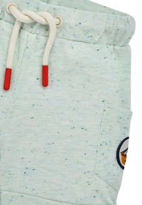 Pantaloni sportivi azzurri chiari con una texture a macchie, dotati di un laccio bianco con punte rosse e una tasca laterale con una toppa circolare.