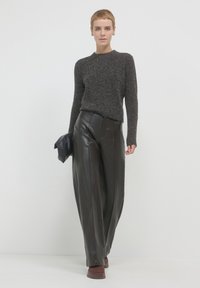 Dunkelgrauer gestrickter Pullover mit langen Ärmeln, kombiniert mit hochtaillierten schwarzen Lederhosen. Das Modell hält eine schwarze Clutch.