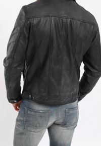 Černá kožená bunda s přiléhavým střihem, viditelnými švy a patkovým zapínáním v pase. Nosená přes modré džíny.