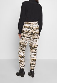 Pantaloni a vita alta strutturati con un audace motivo astratto nero, marrone e bianco, abbinati a un top a maniche lunghe nero e stivali con tacco.