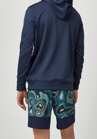 Marinblå hoodie med en texturerad finish, tillsammans med mönstrade badshorts i grönt, blått och svart. Shortsen har en enfärgad marinblå midja.