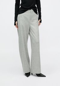 Grå teksturerede bukser med vide ben og en glat finish, med en tætsiddende talje og kombineret med sorte spidse hæle.