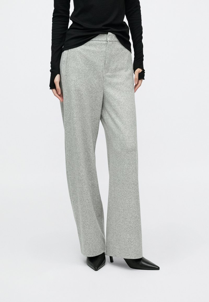 Grå teksturerede bukser med vide ben og en glat finish, med en tætsiddende talje og kombineret med sorte spidse hæle.