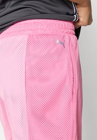 Roosa võrgusilm joggerid elastse vöökohtaga, millel on hõbedane Puma logo ja hingav, tekstureeritud kangas.
