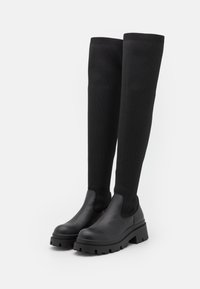 Polkupyöriin yltävät mustat saappaat, joissa on teksturoitu neulottu varsi ja sileä nahkakärki, sekä paksu kumipohja, jossa on karhea pintakuvio.