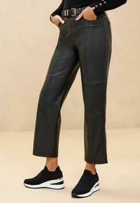 Pantalons en simili cuir noir avec un design à jambe droite, présentant une taille haute et des détails de couture subtils, associés à des baskets compensées noires.