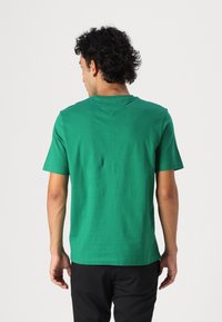 T-shirt en coton vert, à manches courtes, col rond. Design simple avec une texture lisse et un ourlet droit, vu de dos.