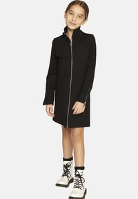 Abito nero con zip, maniche lunghe e polsini a coste, abbinato a stivaletti bianchi con lacci, dettagli neri e suole spesse.