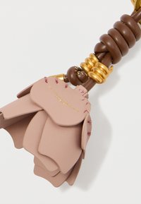 Ādas atslēgu piekariņš ar rozā ziedu dizainu, brūniem ādas akcentiem, zelta aparatūru un redzamām šuvju detaļām.