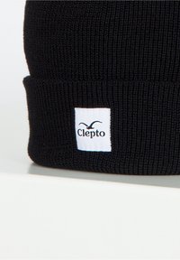 Schwarze gestrickte Mütze mit umgeschlagenem Bündchen und einem weißen rechteckigen Etikett, das ein schwarzes Logo zeigt, das einem Vogel ähnelt.