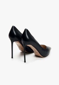 Zwarte leren hoge hakken met een puntige neuzen en slanke stiletto-hakken. Gladde textuur met een beige binnenvoering en merklogo.