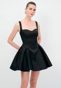 Robe en satin noir avec un corsage ajusté, décolleté carré et larges bretelles, s'évasant en une jupe plissée. Texture lisse avec un design minimaliste.