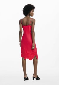 Vestido de satén rojo con tirantes ajustables de espagueti, con detalles de encaje en el dobladillo y un corte ajustado. Combina con sandalias negras de tacón.