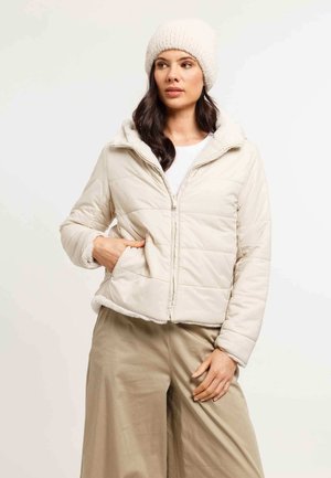Light beige puffer jacket with a soft, textured, fur-lined hood and cuffs. Full zipper, side pockets, and quilted design. Paired with beige pants.