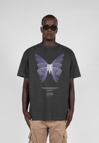 Mørkegrå T-shirt med korte ærmer, der har et stort lilla sommerfugletryk og hvid tekst centreret på brystet, lavet af blødt bomuldsstof.