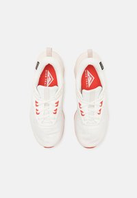 Chaussures de sport blanches avec accents rouges, tige en mesh et design texturé. Équipées de lacets blancs et d'un logo intérieur de marque.