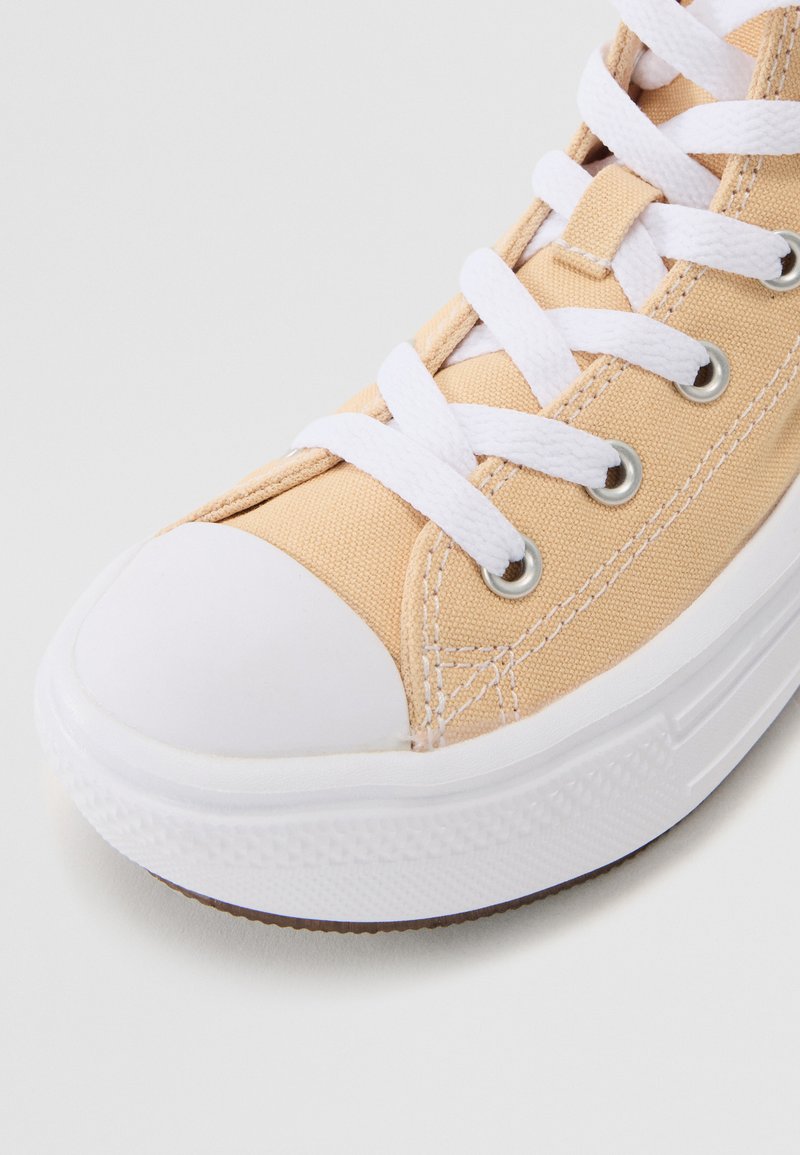 Zapatilla de lona en melocotón claro con puntera y suela de goma blanca. Presenta cordones blancos y ojales plateados. Textura suave.
