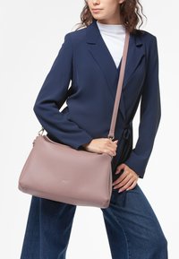 Borsa crossbody in pelle rosa chiaro con una texture liscia, chiusura con zip e tracolla regolabile, esposta su uno sfondo neutro.