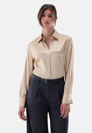 Beige Seidenhemd mit Knöpfen, Kragen und langen Ärmeln, kombiniert mit dunklen, maßgeschneiderten Hosen und einem schwarzen Gürtel. Glatte Textur, klassisches Design.