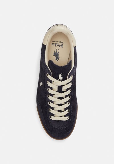 Σουέντ ναυτικό αθλητικό παπούτσι με κρέμ κορδόνια, διαθέτει λαστιχένια σόλα και μικρό κεντημένο λογότυπο πόλο. Μαλακή υφή και κομψός σχεδιασμός.