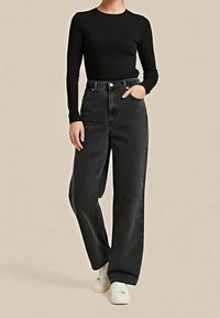 Top negro de manga larga combinado con jeans negros de tiro alto y corte holgado. Detalles notables incluyen bolsillos delanteros y una textura suave.