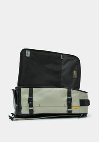 Zaino grigio e nero con una cerniera aperta, dotato di spallacci, una superficie liscia e un'accortezza gialla. Lo spazio interno è scuro.