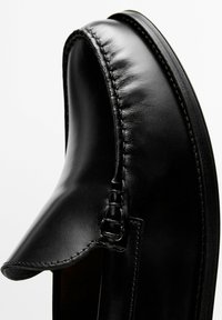 Scarpa elegante in pelle nera senza lacci con cuciture dettagliate intorno alla punta e finitura liscia e lucida.