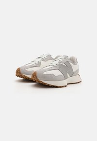 Chaussures de sport grises et blanches avec un dessus texturé, présentant un design distinct, des lacets et une semelle en caoutchouc avec des motifs circulaires.