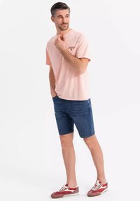 Camiseta de manga corta de color rosa claro con un logo en el pecho, combinada con shorts de mezclilla azul y zapatillas rojas con detalles blancos.