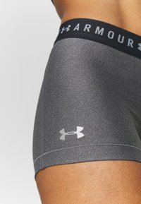 Pantaloni corti atletici grigi con una vita con logo nero. Presentano una texture liscia e un design aderente. Emblema del marchio argentato in basso a destra.