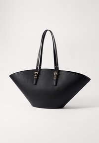 Sort læder tote bag med en bred, trekantet form. Har to lange håndtag og spænde detaljer på siden, glat tekstur.