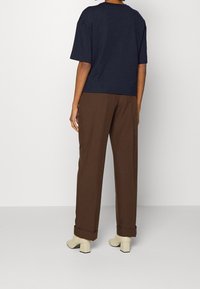 Námořnické tričko s krátkým rukávem spárované s hnědými širokými kalhotami a smetanovými botami na nízkém podpatku. Viditelný zakroucený lem na kalhotách.