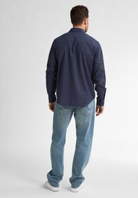 Navy-paitapaita suoran helman kanssa, yhdistettynä vaaleansinisiin farkkuihin. Ominaisuuksiin kuuluvat pitkät hihat ja farkuissa kontrastivärinen tikkaus.