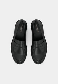 Mocassins noirs en cuir à enfiler avec un détail de bride penny, bout arrondi et coutures visibles, placés côte à côte sur fond blanc.